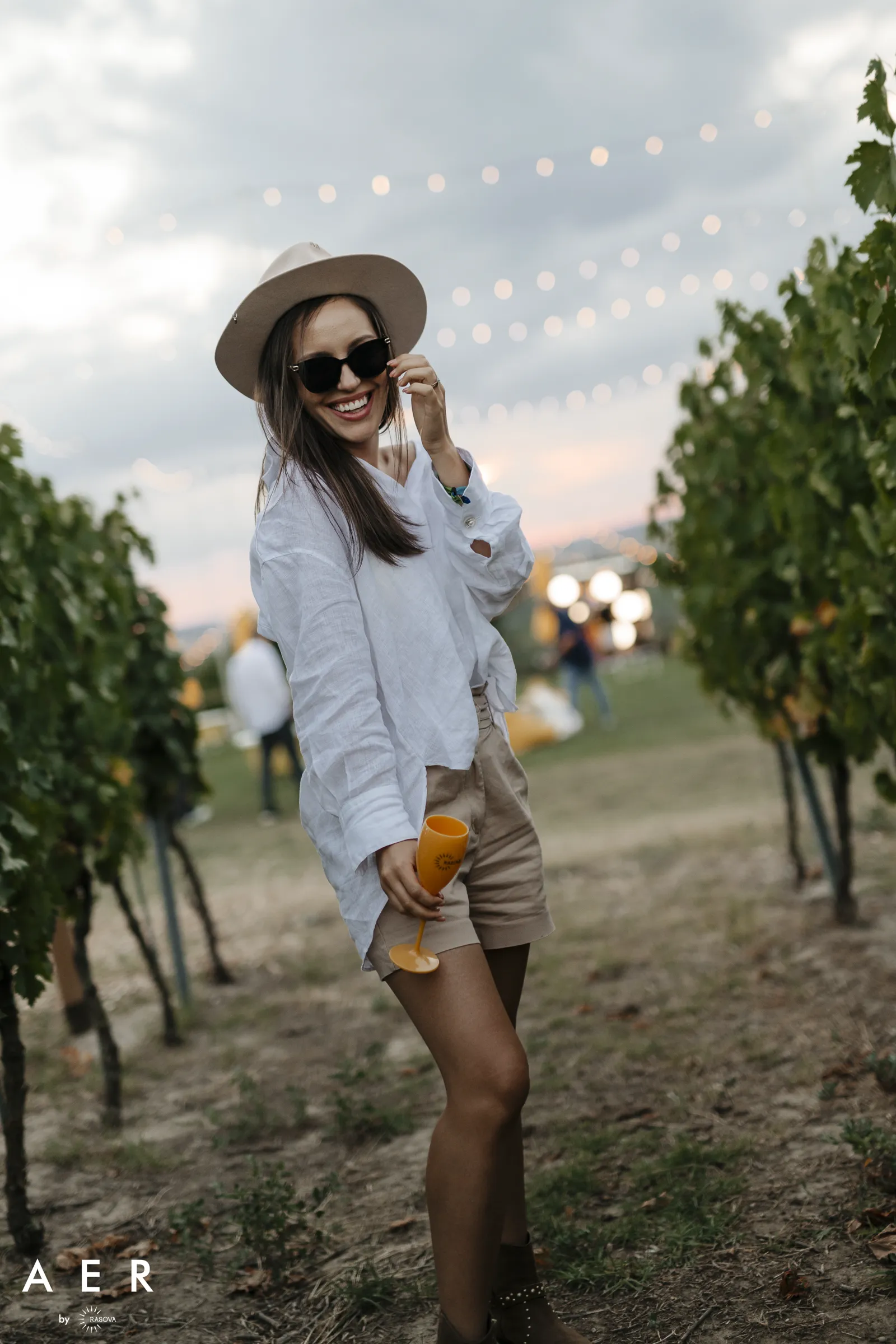 A guest with a Rasova glass among the vine rows, under the lights, at AER by Rasova